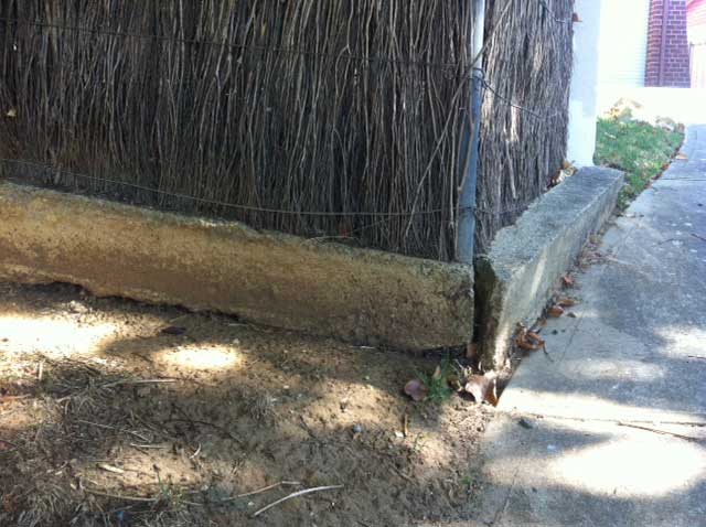 Image:   The concrete base has not been reinforced and has moved with ground or tree root movement.  The small end section at least should be replaced with a new fence.